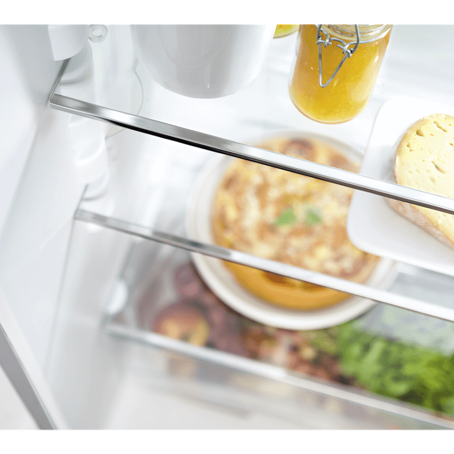 Inside a fridge: jar of jam, quiche, bread slice, and other food items. Glass shelves and a white interior are visible.