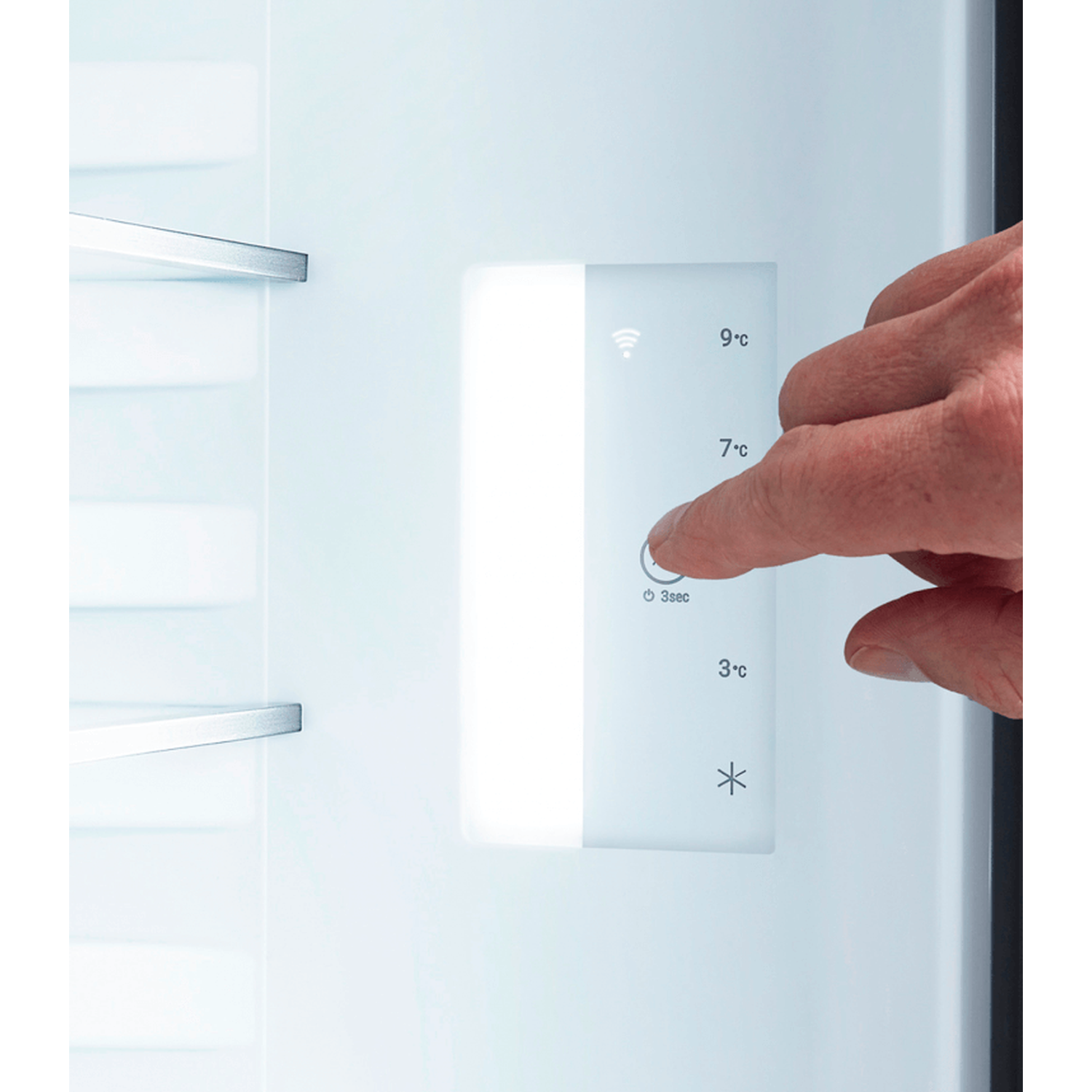 A hand presses a button on a fridge control panel. The panel displays temperature settings and a Wi-Fi symbol.