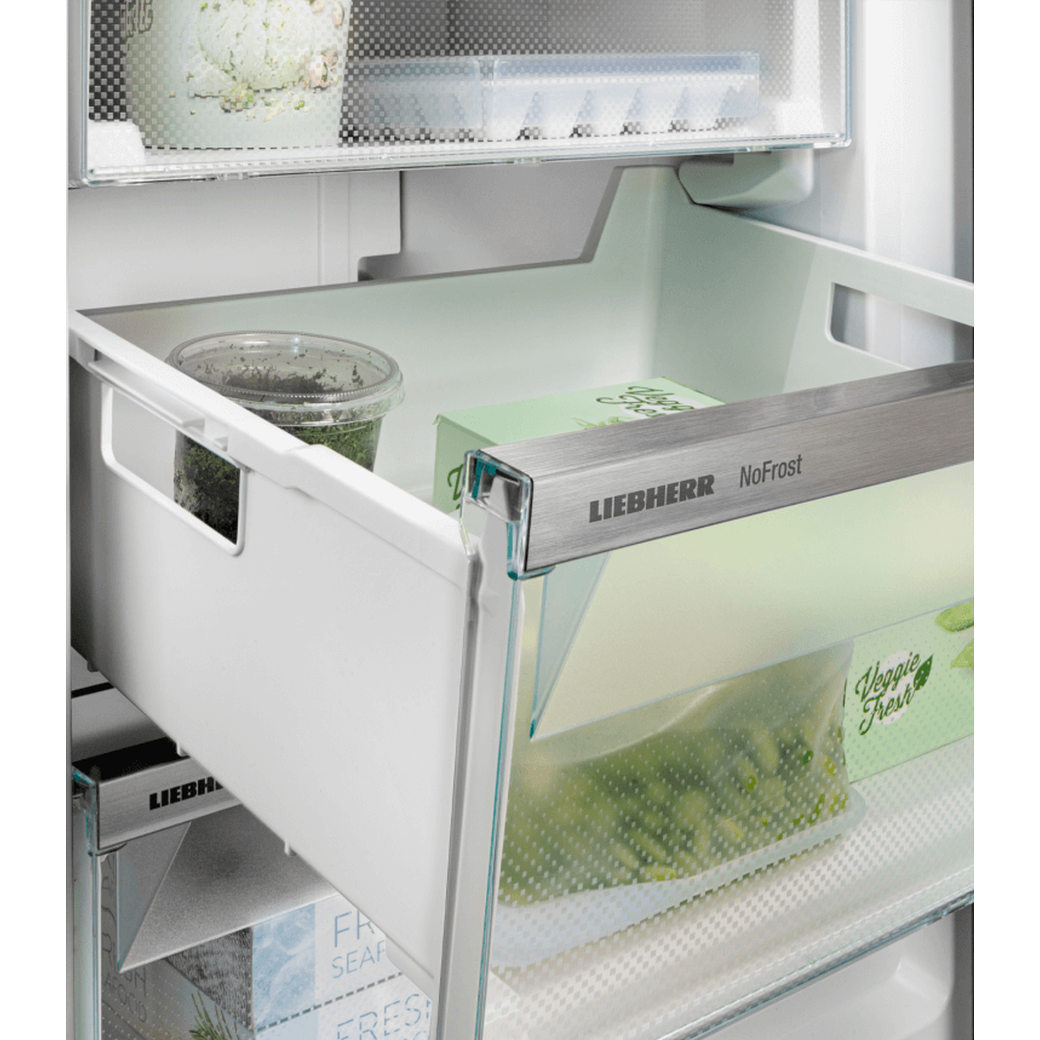 Inside a fridge: a drawer with vegetables and herbs, labeled 'Liebherr NoFrost'. Clear plastic containers are visible.