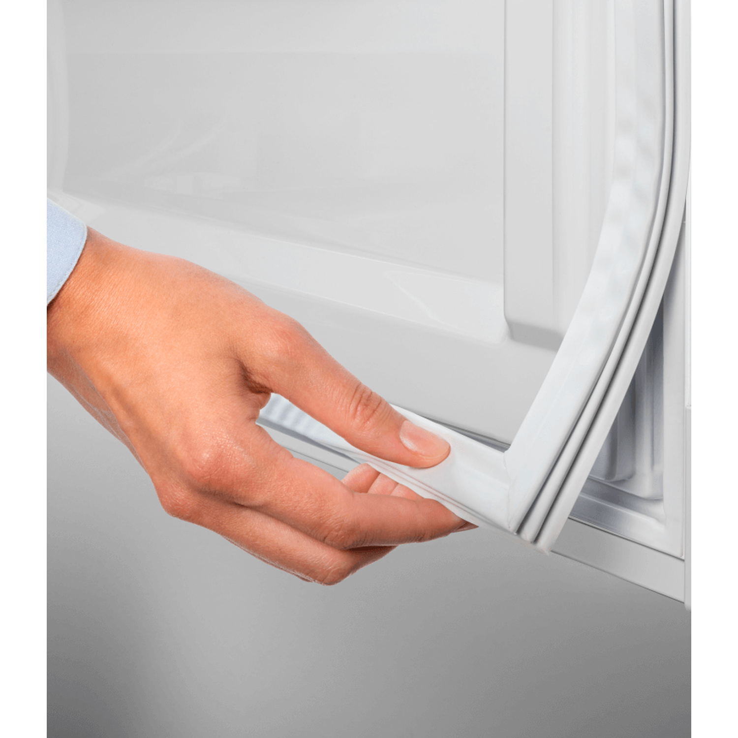 A hand pulls a white rubber seal from a white refrigerator door. The background is a white appliance.