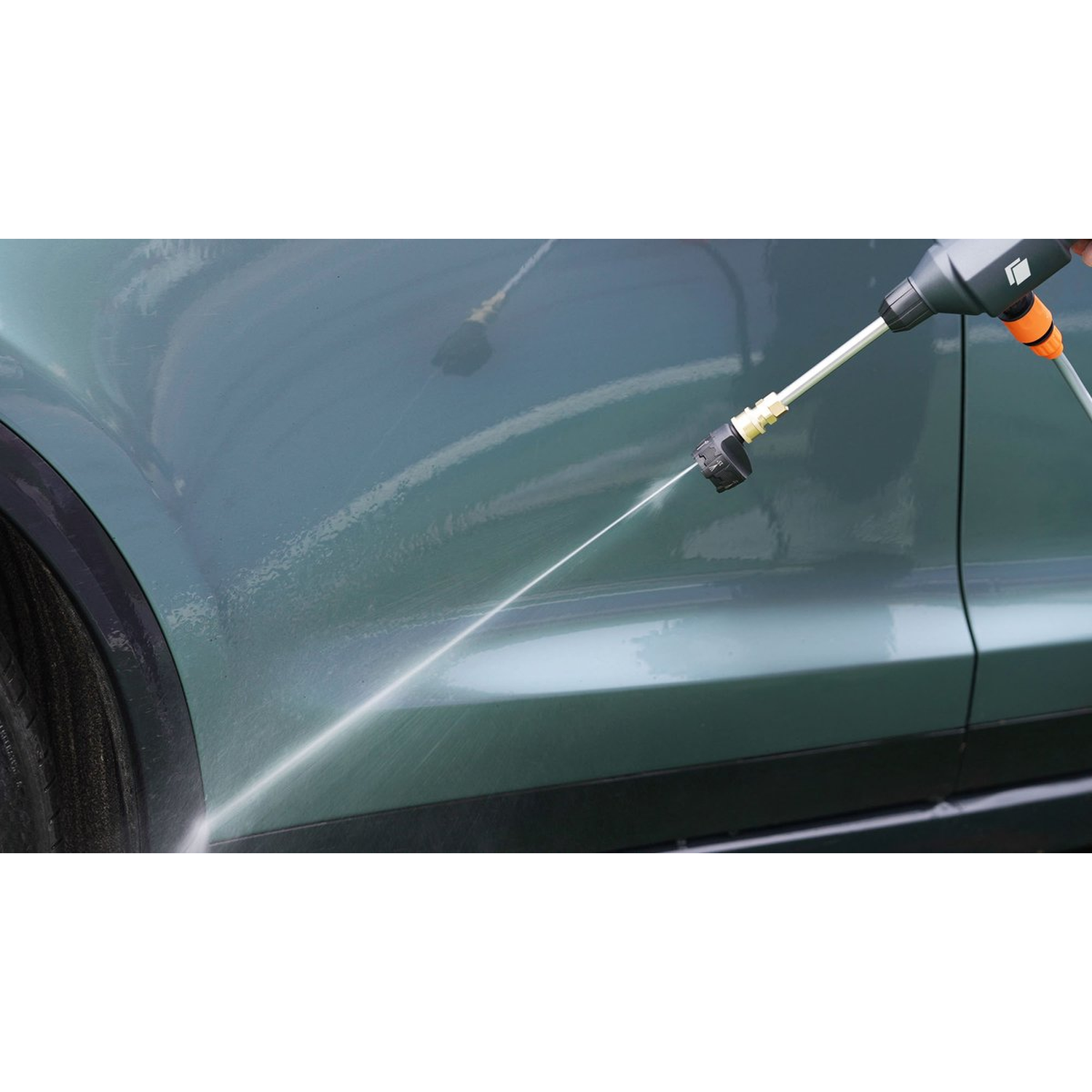 A car is being washed with a pressure washer. Water is spraying onto the green car's side.