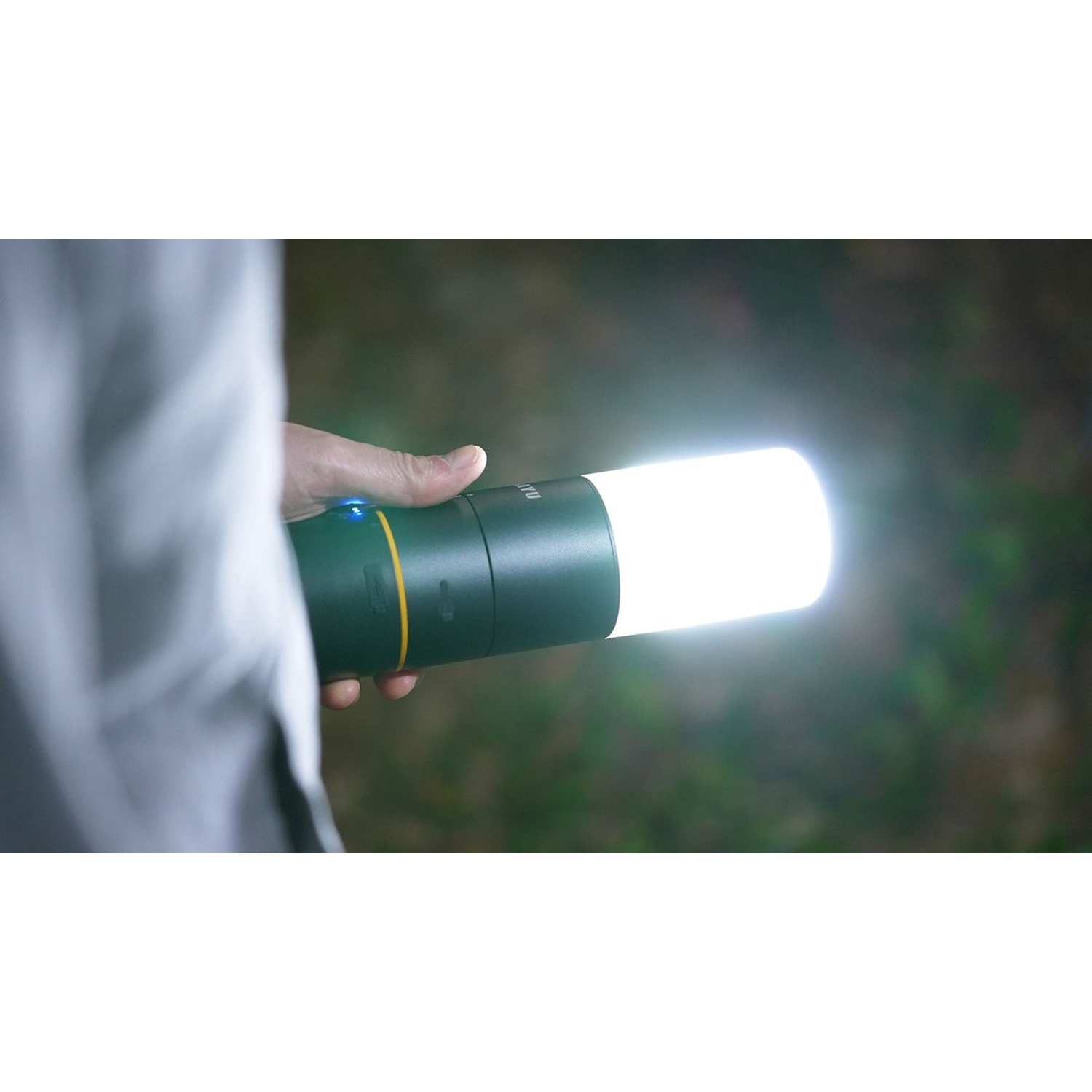 Een persoon houdt een groene zaklamp vast met helder wit licht. De achtergrond is wazig groen gebladerte.