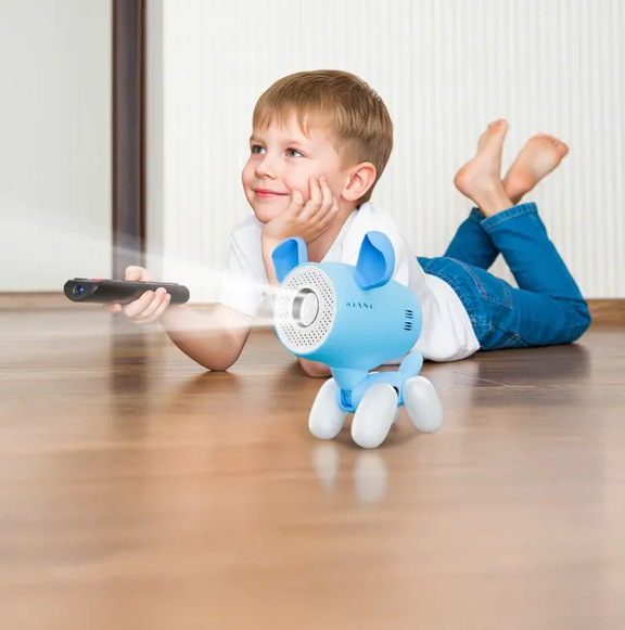Chłopiec leży na podłodze i patrzy na projektor w kształcie psa. Trzyma pilota. Projektor jest niebieski i wyświetla światło.