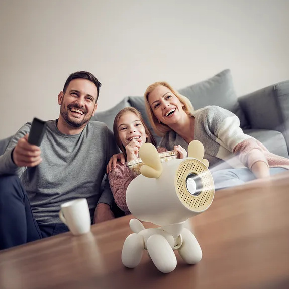 Rodzina ogląda film. Projektor w kształcie psa wyświetla film. Jedzą popcorn i się uśmiechają.