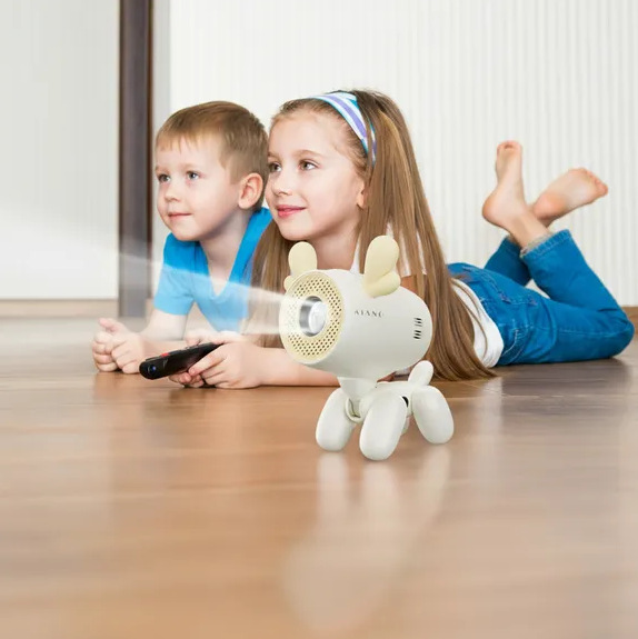 Dwoje dzieci ogląda ekran, jedno trzyma pilota. Biały projektor w kształcie psa stoi na podłodze.
