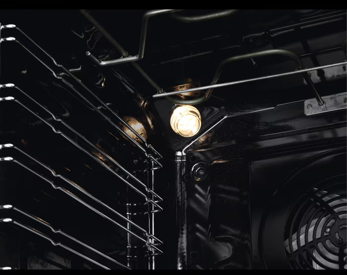 Innenansicht eines Ofens. Ofenlicht leuchtet, beleuchtet die Roste. Ein Ventilator ist unten rechts sichtbar. Der Innenraum ist dunkel.