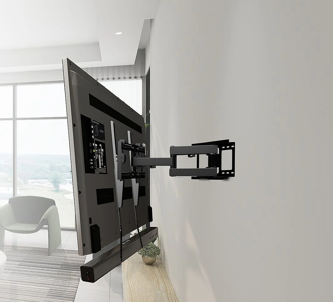 Duży telewizor zamontowany na ścianie z obrotowym ramieniem. Pod telewizorem soundbar. W tle okno i krzesło.