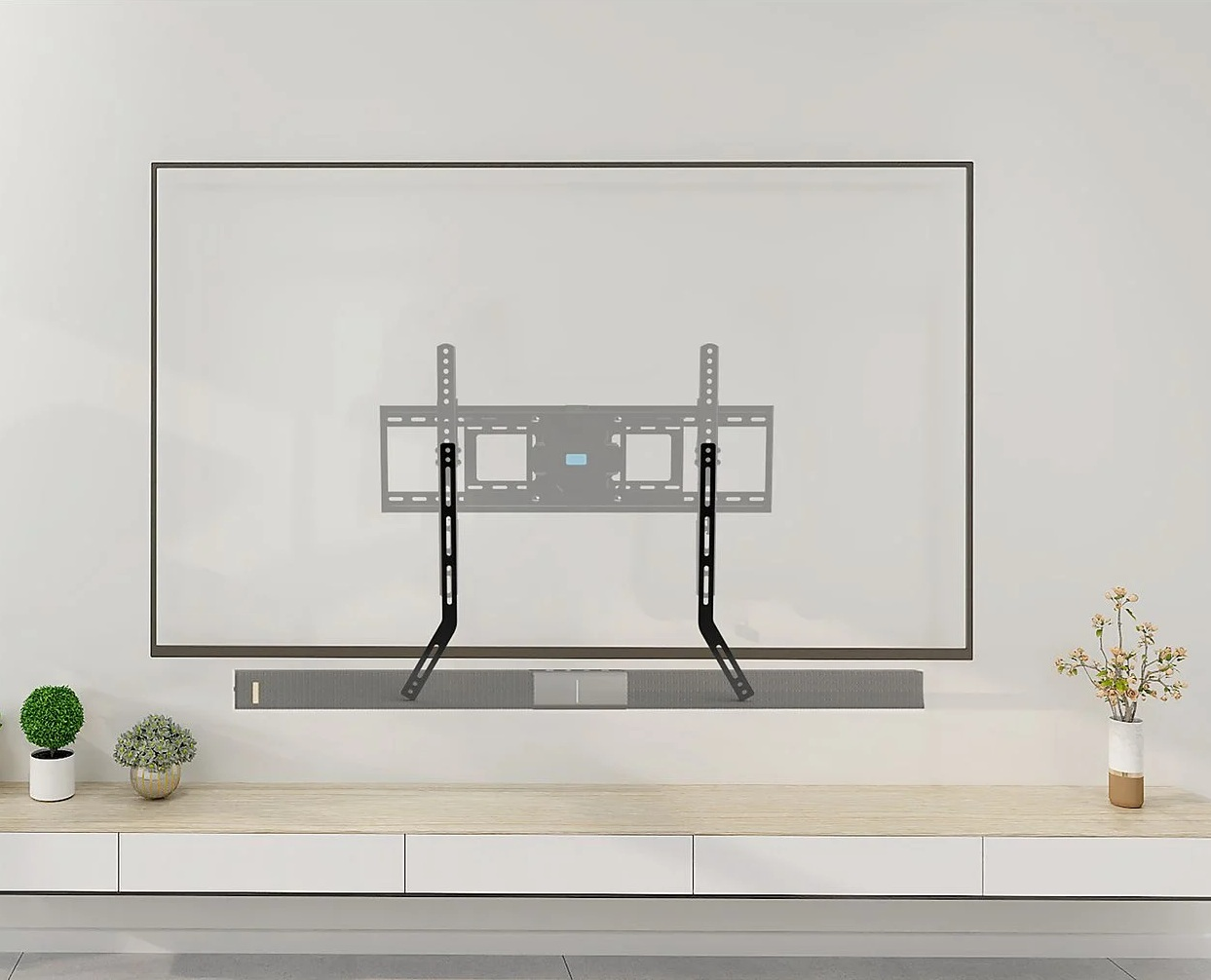 Stojak pod telewizor z soundbarem. Czarny uchwyt na białej ścianie. Drewniana szafka z roślinami i kwiatami na pierwszym planie.