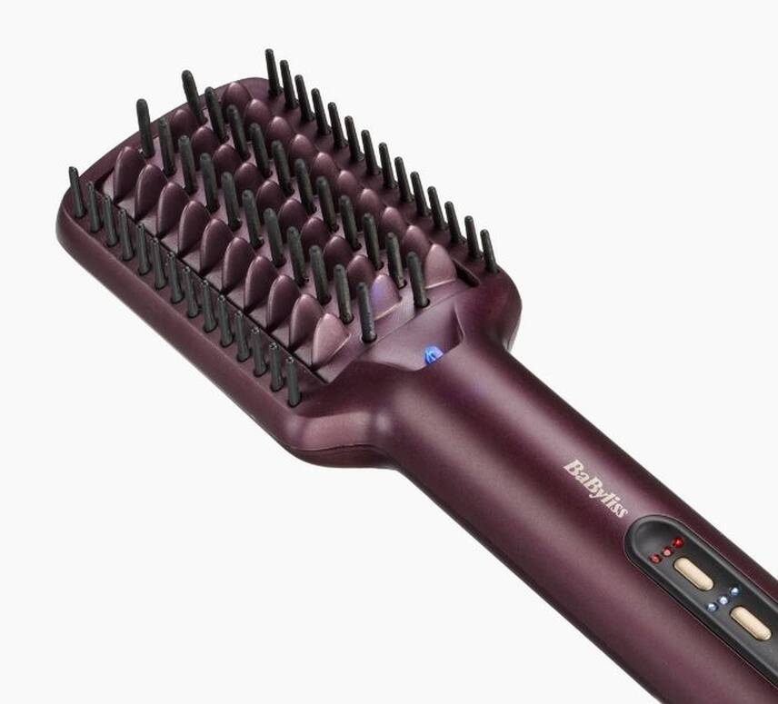 Une brosse lissante Babyliss violette. Elle a des poils noirs et un interrupteur marche/arrêt. Le fond est blanc.