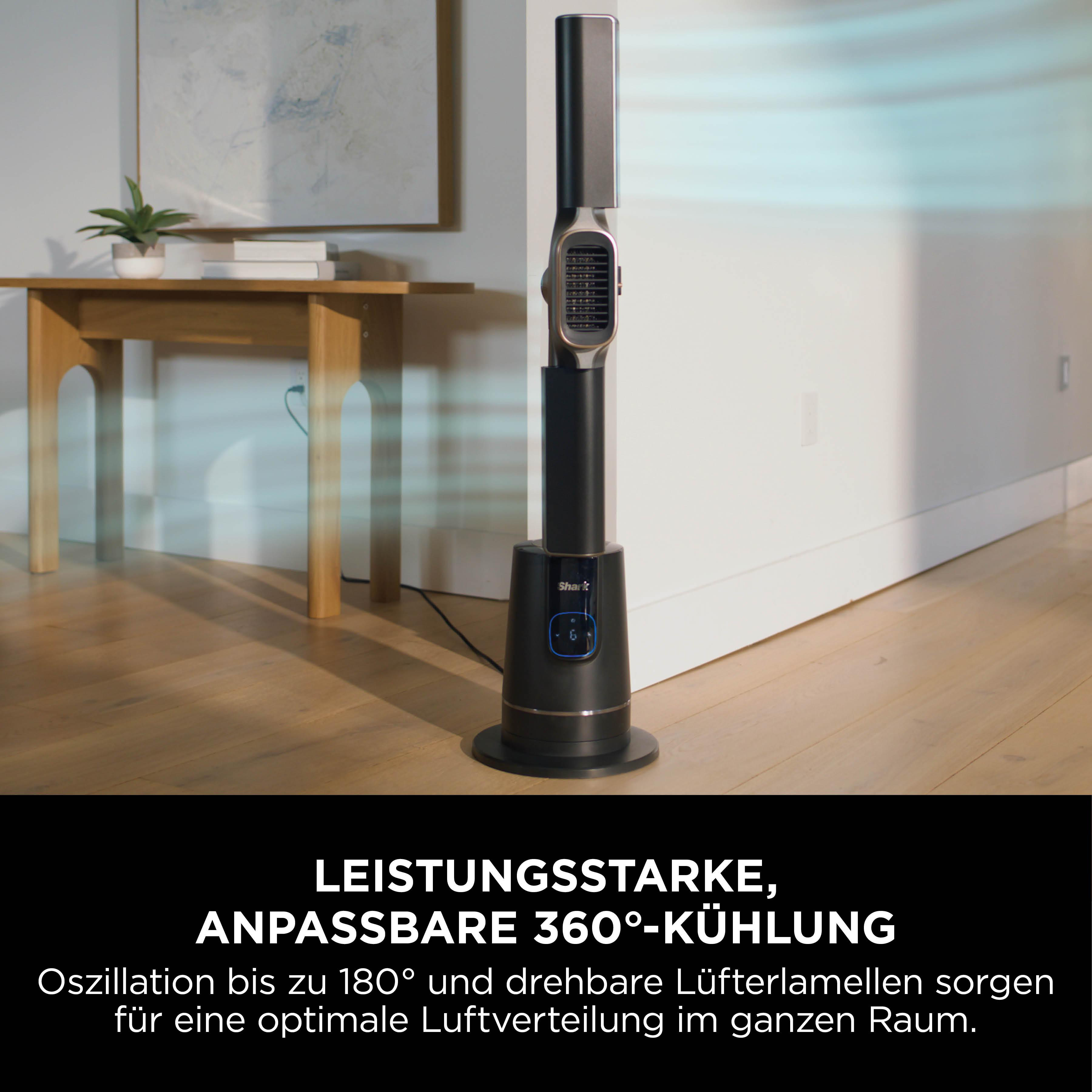 Ein schwarz-silberner Ventilator steht in einem Raum. Ein Tisch und ein Gemälde sind im Hintergrund.