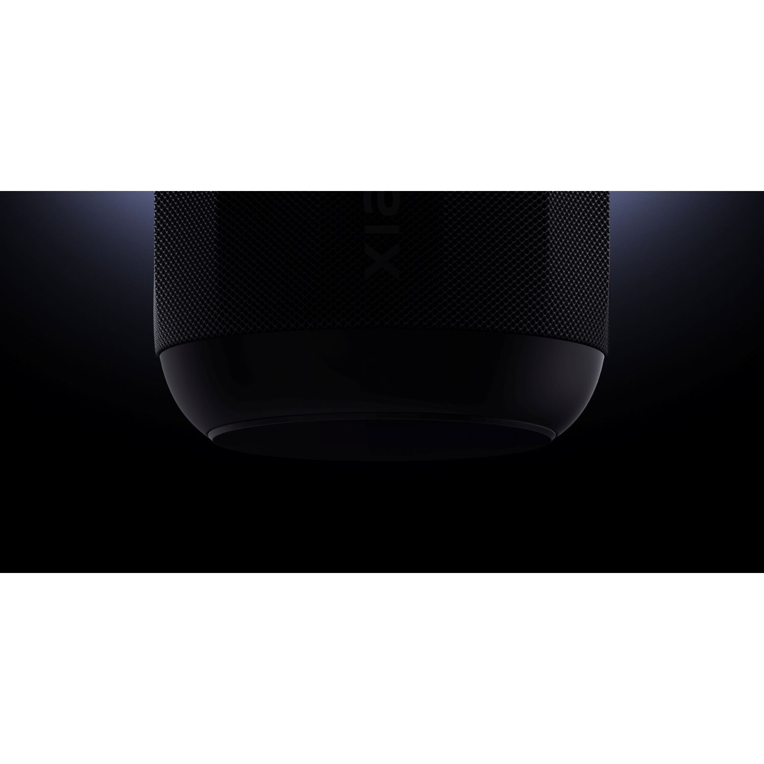 A black speaker against a dark background. The top has a textured surface, and the bottom is smooth and rounded.