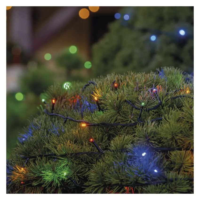 Egy zöld bokor közeli képe színes füzérfényekkel díszítve. Néhány fény fókuszban van. A háttér elmosódott fényekkel rendelkezik.