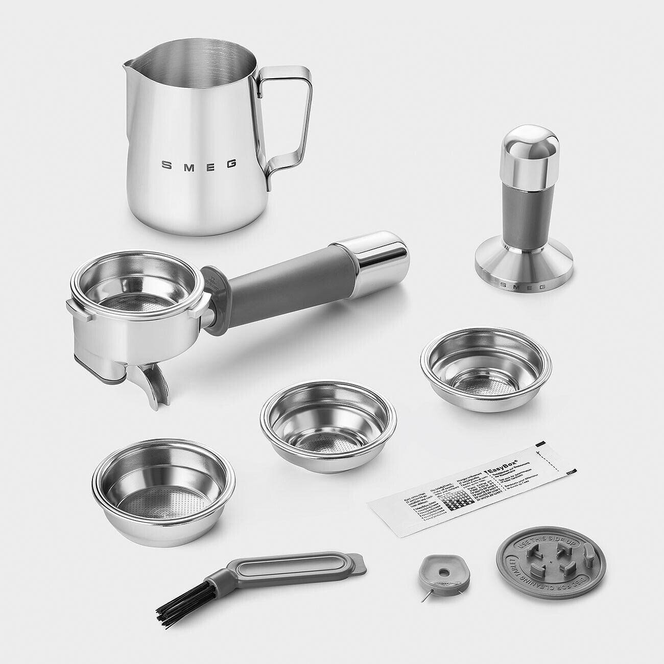 Kaffeemaschinenzubehör: Kännchen, Siebträger, Tamper, Filterkörbe, Bürste, Reinigungswerkzeuge und ein Päckchen.