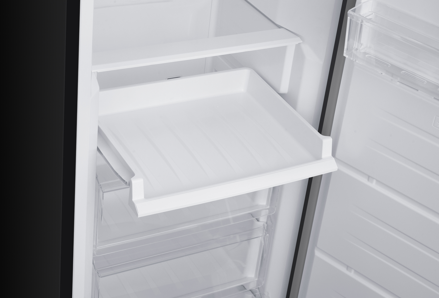 Interior de refrigerador abierto con estantes blancos y una bandeja extraíble. Cajones de plástico transparente debajo. Lado negro visible.
