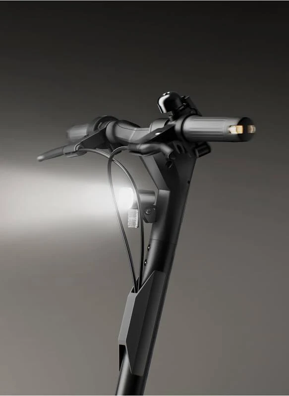 Primer plano del manillar de un patinete eléctrico negro con luces. Una luz brilla intensamente en la parte delantera. Una campana está montada en la barra.