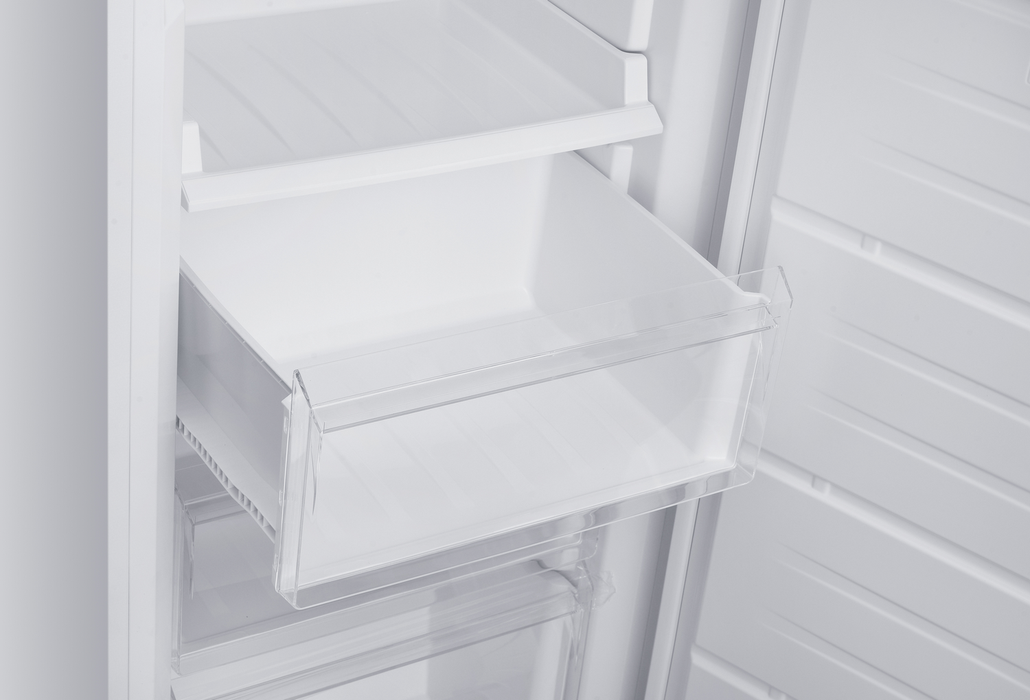 Dentro de un refrigerador blanco, un cajón transparente está extraído. Se ven otros estantes blancos y el interior del refrigerador.