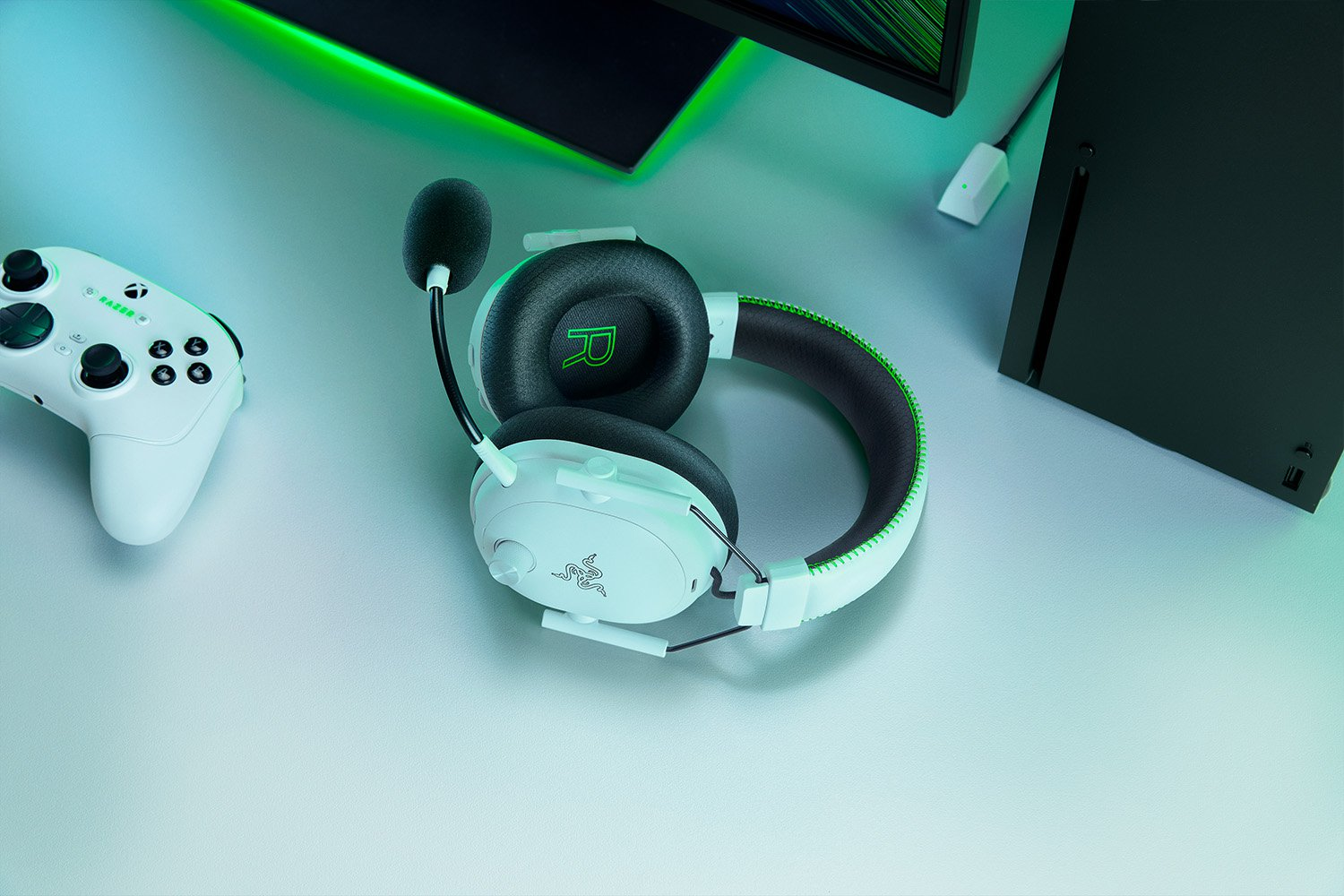 Casque blanc avec micro, manette et console noire sur surface grise. Accents et éclairage verts.