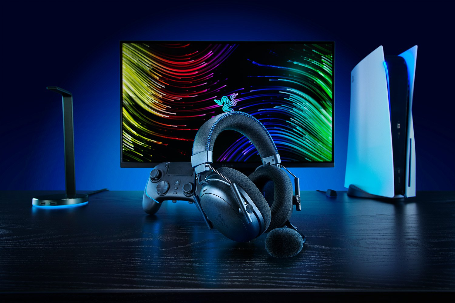 Configurazione di gioco. Cuffie, controller, monitor con linee colorate, PS5 e supporto su superficie in legno scuro.