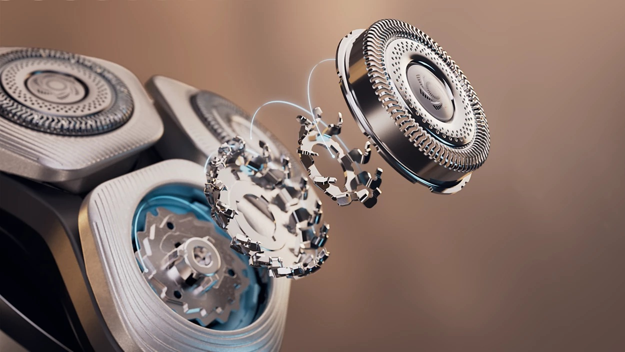 Zbliżenie rozebranej golarki elektrycznej. Widoczne ostrza i mechanizmy wewnętrzne, na brązowym tle.