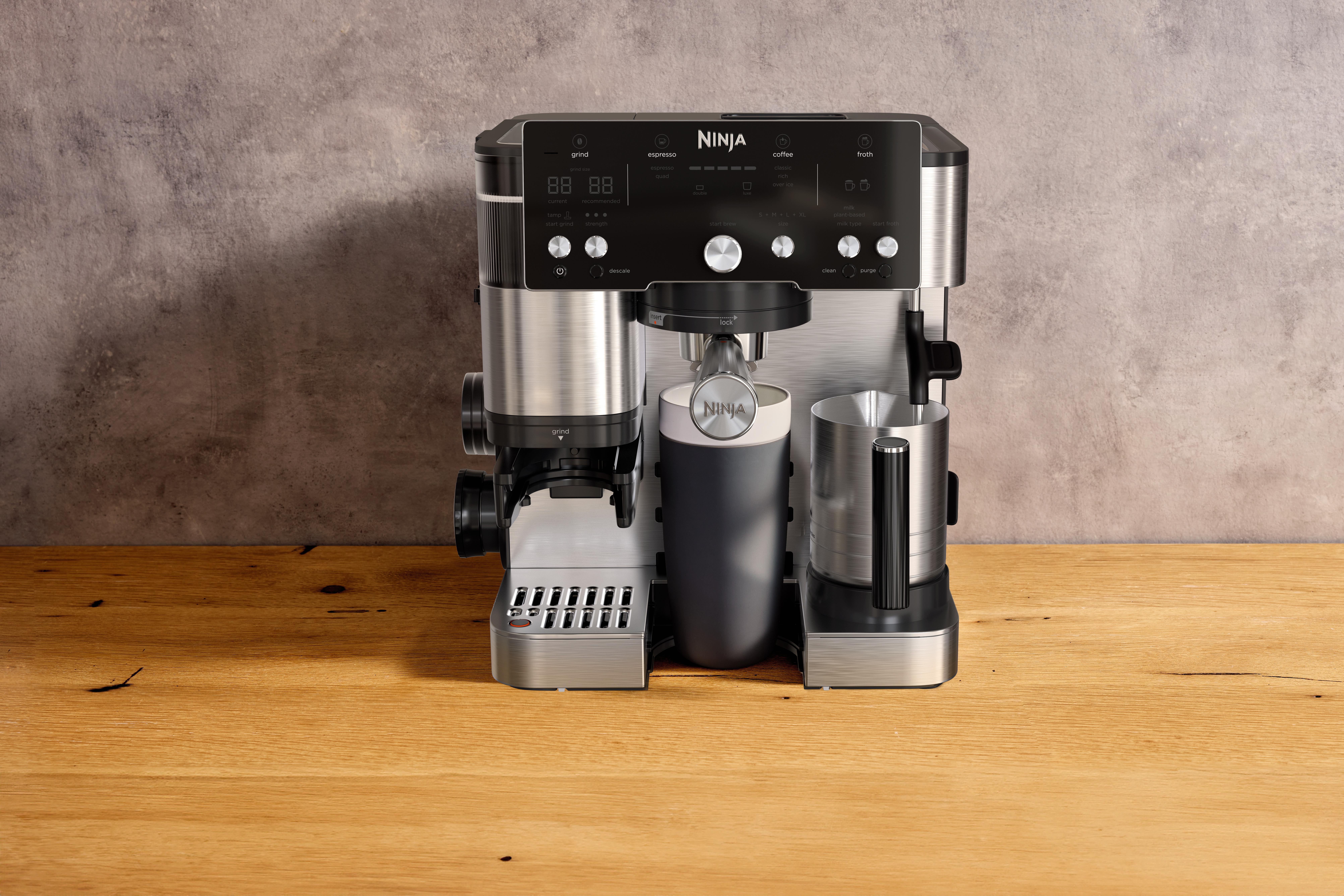 Eine Ninja-Kaffeemaschine steht auf einer Holzoberfläche. Sie hat ein schwarzes Bedienfeld mit verschiedenen Knöpfen und ein Edelstahlgehäuse.