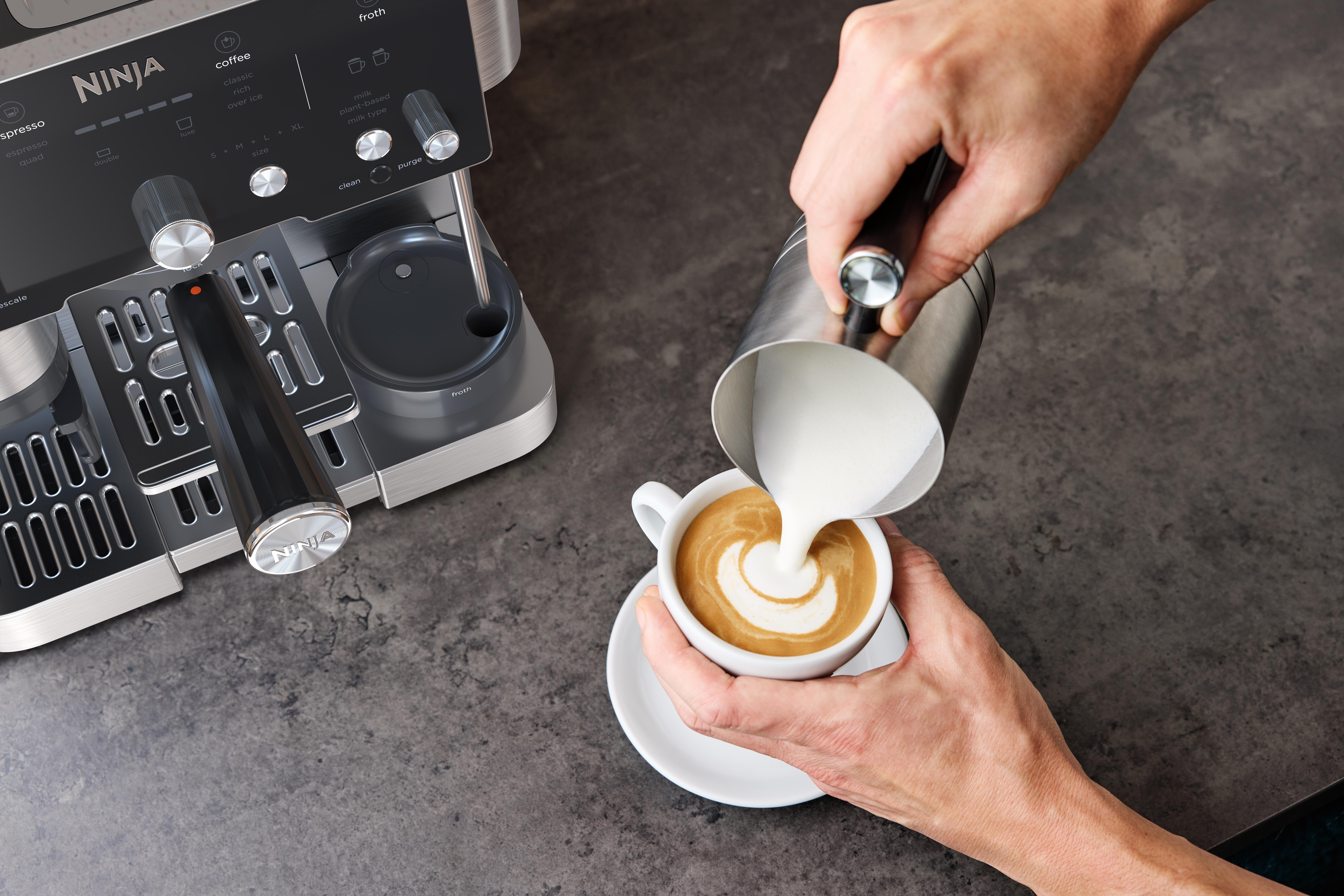 Eine Person gießt Milch in eine Kaffeetasse und kreiert Latte Art. Eine Ninja-Kaffeemaschine ist im Hintergrund.