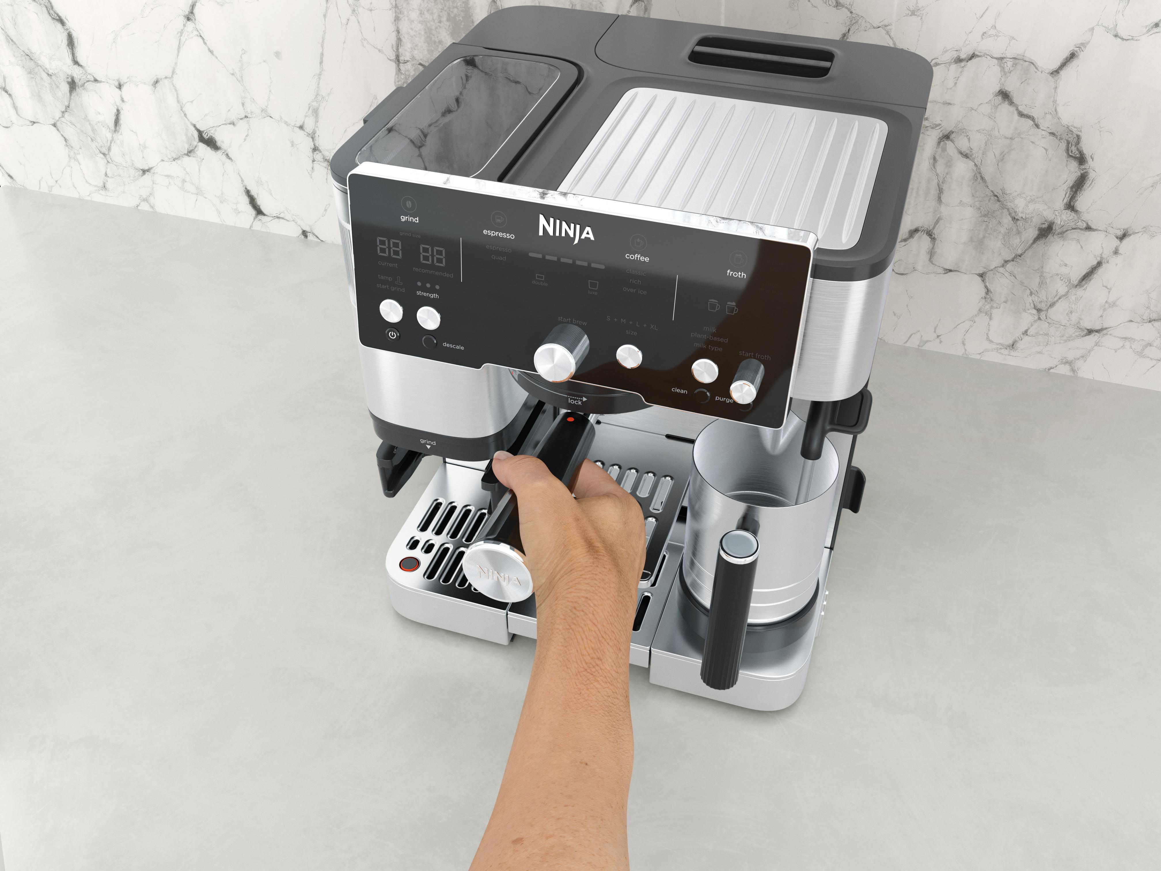 Eine Ninja-Kaffeemaschine steht auf einer Theke. Eine Hand legt einen Filter ein. Der Hintergrund hat einen Marmoreffekt.