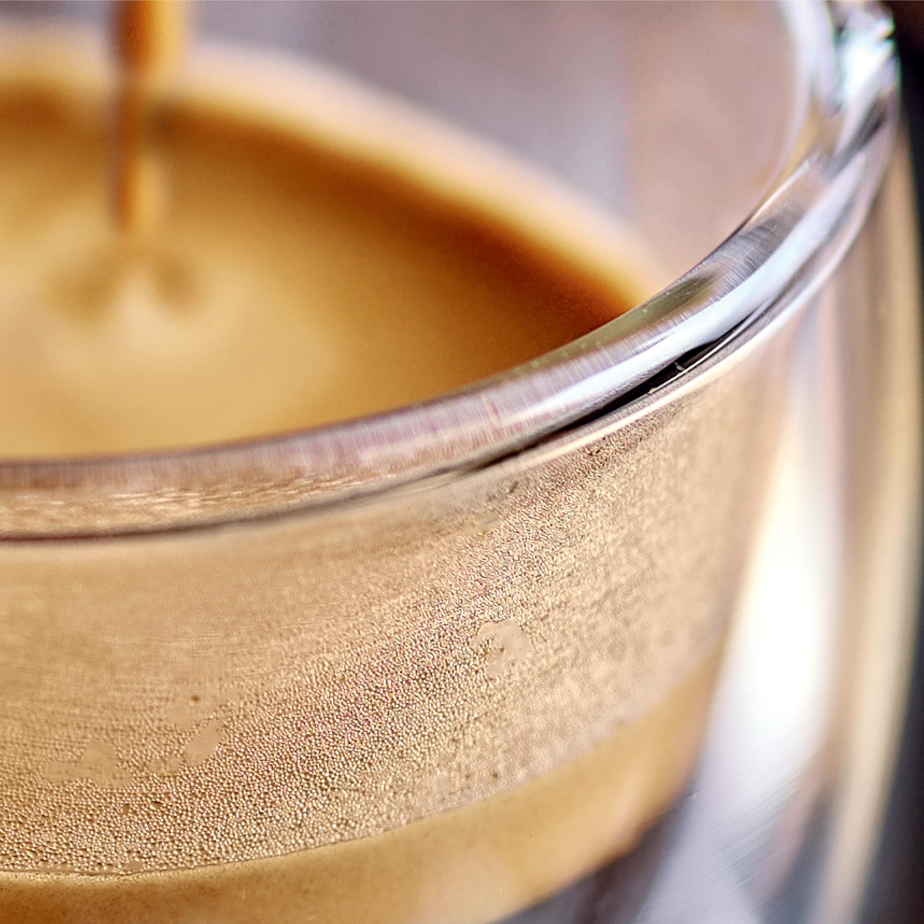 Nahaufnahme eines mit Kaffee gefüllten Glases. Dampf kondensiert am Glas. Der Kaffee ist braun.