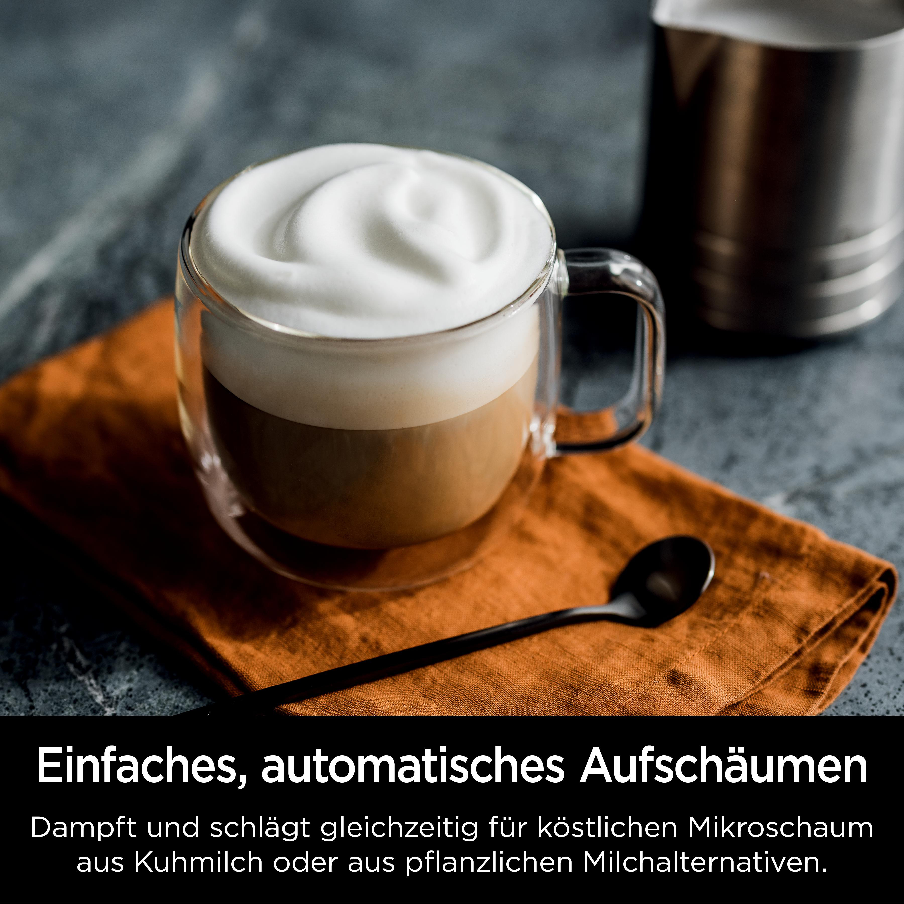 Ein Glas Latte mit Schaum auf einer orangefarbenen Serviette. Ein schwarzer Löffel liegt daneben.
