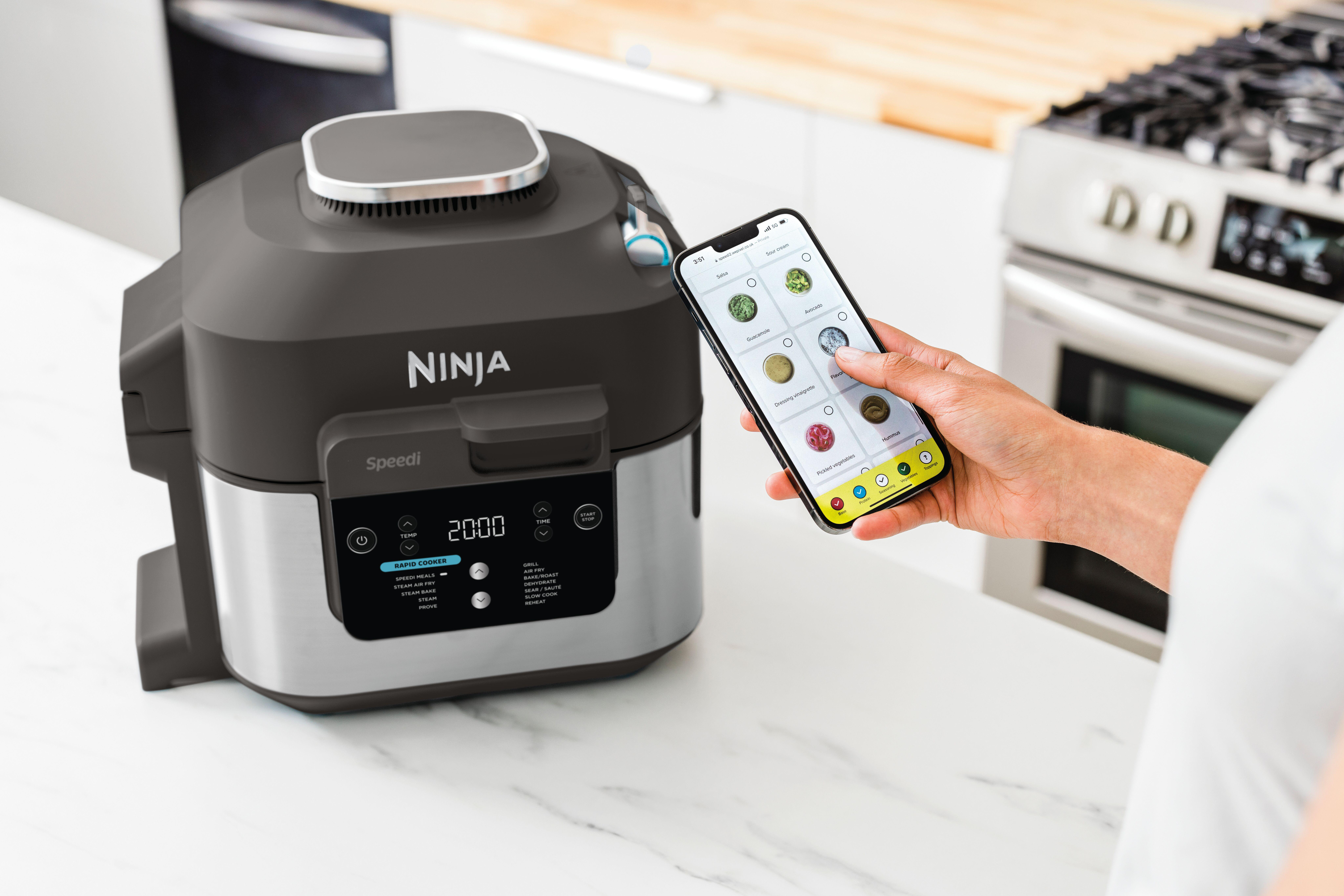 Ein Ninja Speedi-Kocher steht auf einer Theke. Eine Hand hält ein Telefon mit Essensoptionen.