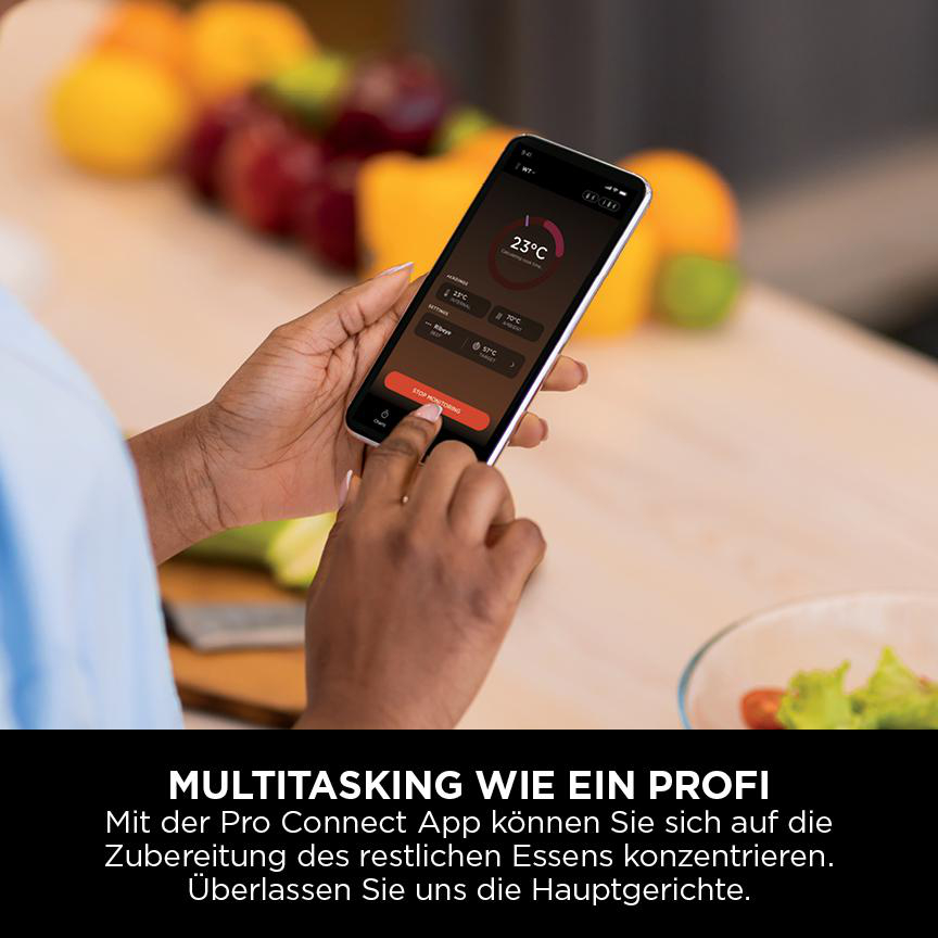 Eine Person hält ein Smartphone mit einer Koch-App. Obst und Gemüse liegen im Hintergrund auf einer Holzoberfläche.