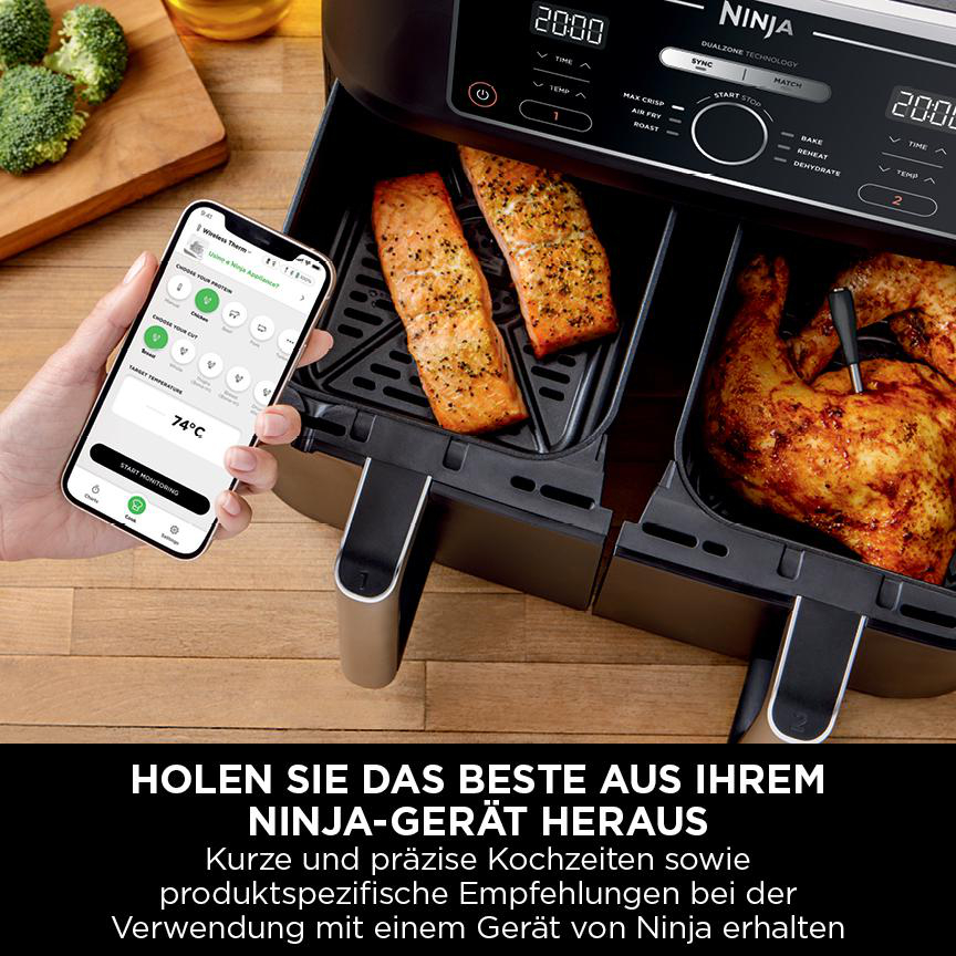 Ein Airfryer mit Lachs und Hähnchen, ein Telefon, das 74 Grad anzeigt, und Brokkoli auf einer Holzoberfläche.