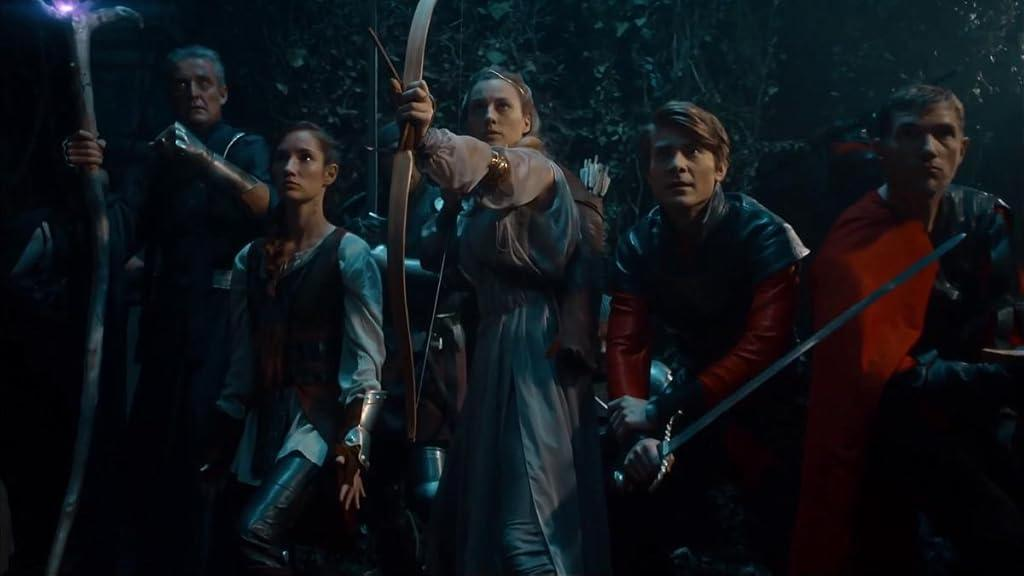 Gruppe von Menschen in Fantasy-Kleidung, einige mit Waffen, in einem Wald. Einer zielt mit einem Bogen, andere halten Schwerter und einen leuchtenden Stab.