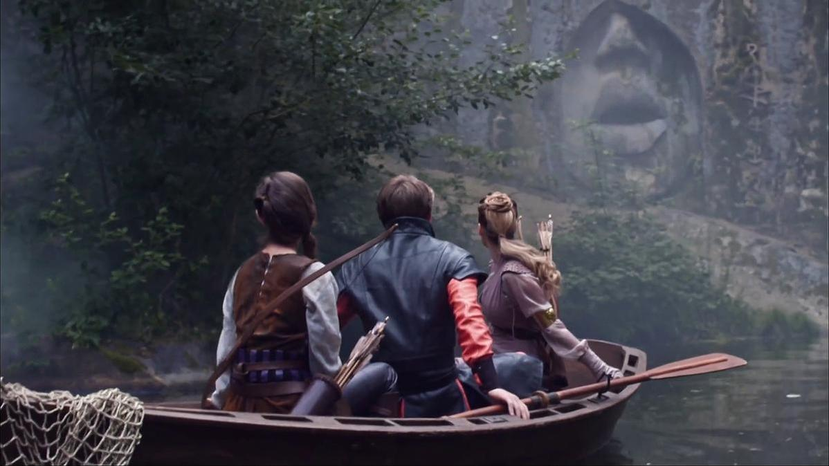Drei Personen in einem Boot auf dem Wasser, abgewandt. Ein großes Gesicht in den Felsen geschnitzt im Hintergrund. Bäume umgeben die Szene.