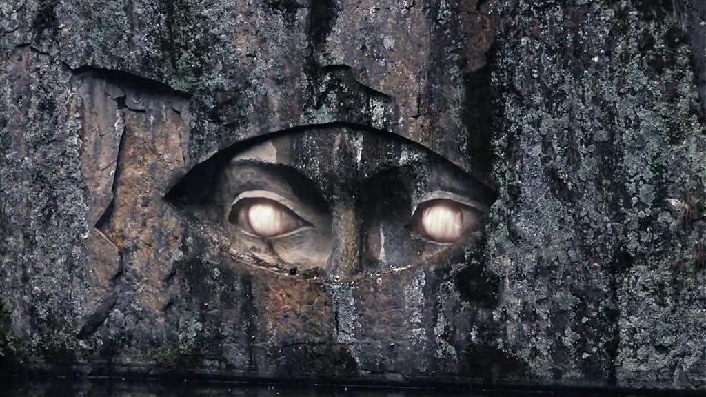 Skulptur von Augen in Felsen gemeißelt. Die Augen leuchten. Dunkler Fels umgibt das geschnitzte Gesicht.