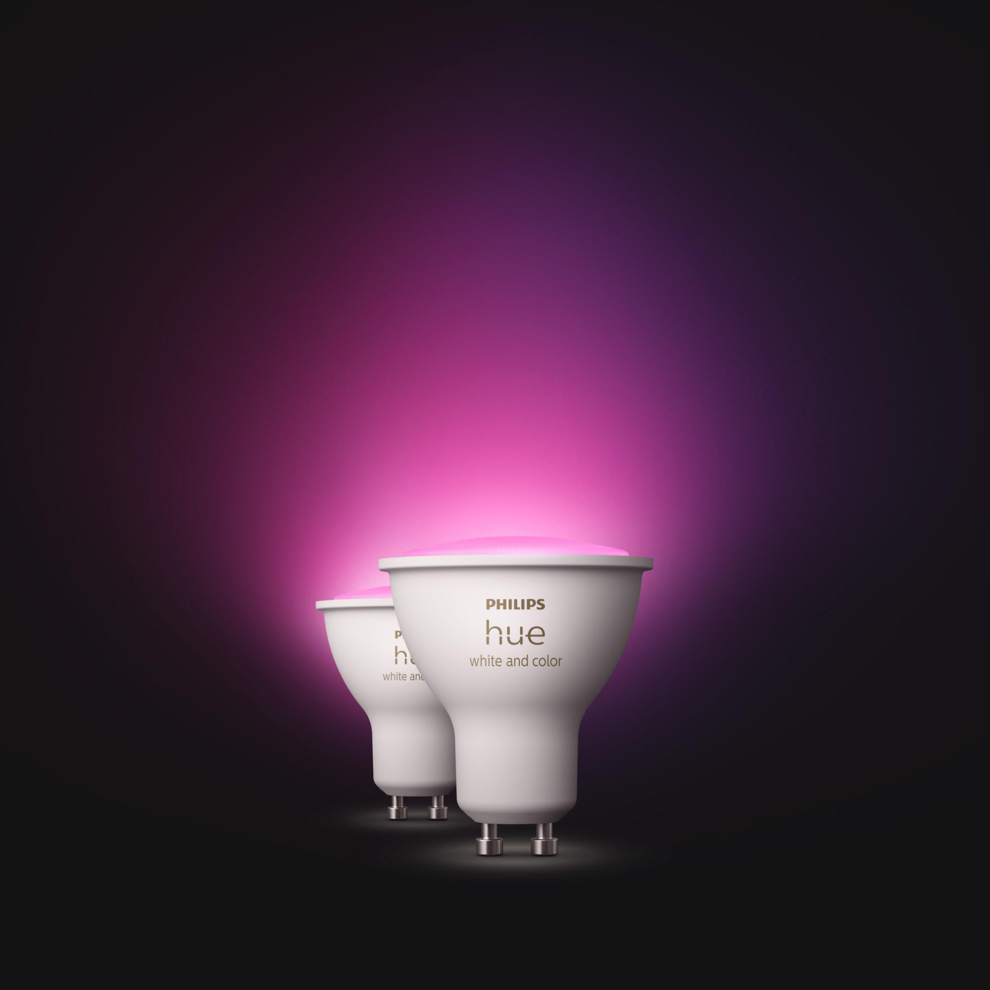 Zwei weiße Philips Hue Smartlights mit rosa Leuchten, vor einem Hintergrund mit lila und schwarzen Farbverläufen.