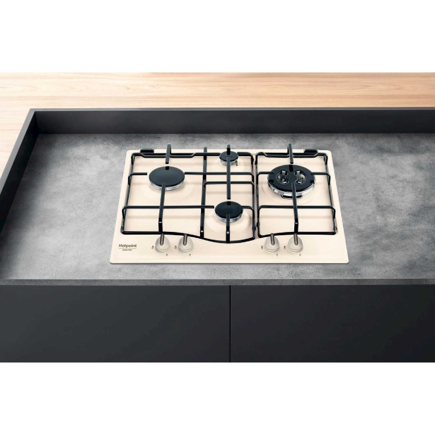 Un piano cottura a gas beige con bruciatori neri e griglia nera è posto su un piano di lavoro grigio. Sullo sfondo una superficie in legno chiaro.