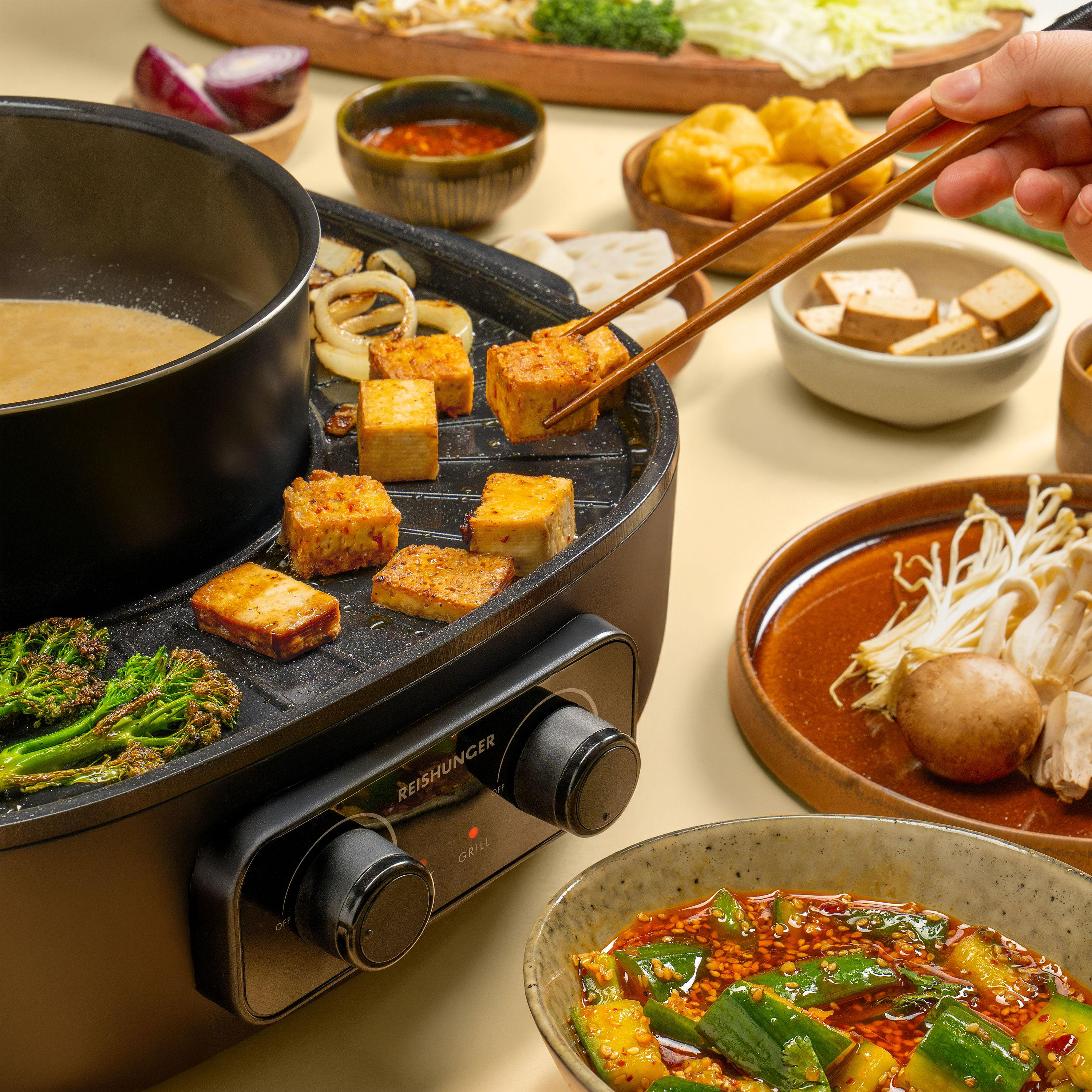 Ein Hot-Pot-Essen mit gegrilltem Tofu, Gemüse und Dipsaucen. Essstäbchen halten Tofu. Nahaufnahme mit verschiedenen Speisen.