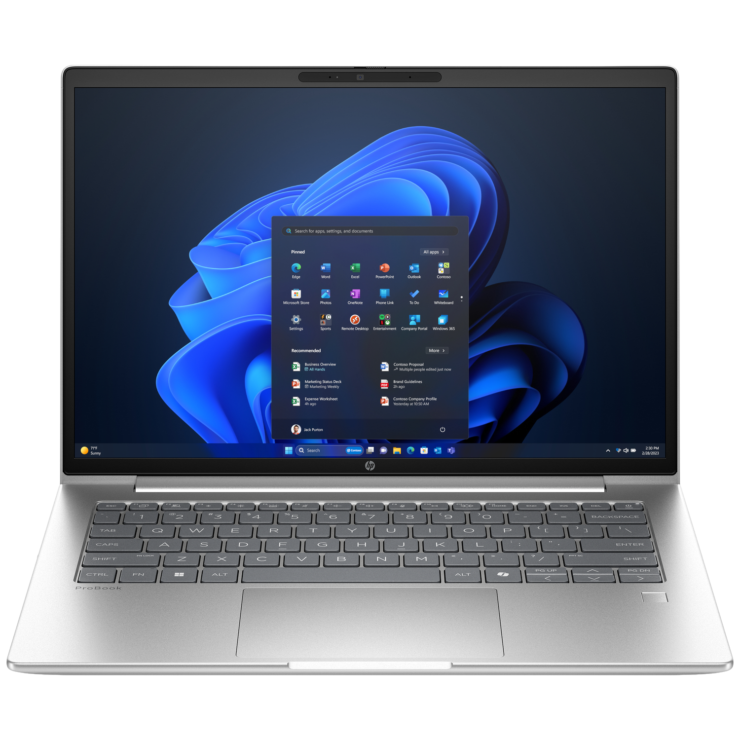 Ordinateur portable argenté avec interface Windows 11 ouverte. Clavier visible sous l'écran. L'écran affiche des icônes et une barre de recherche.