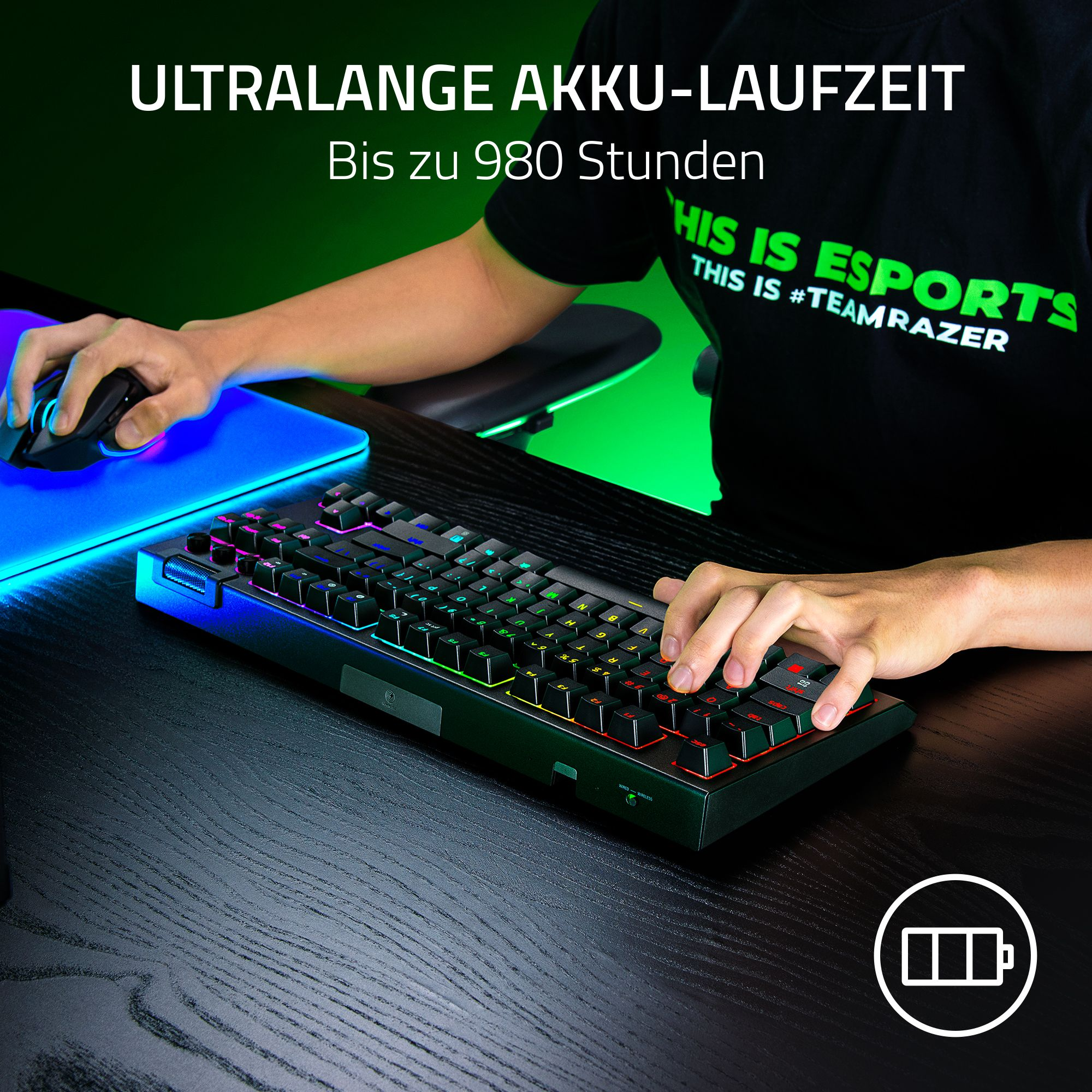 Eine Person benutzt eine Tastatur und Maus. Die Tastatur hat bunte Tasten und liegt auf einem schwarzen Tisch.