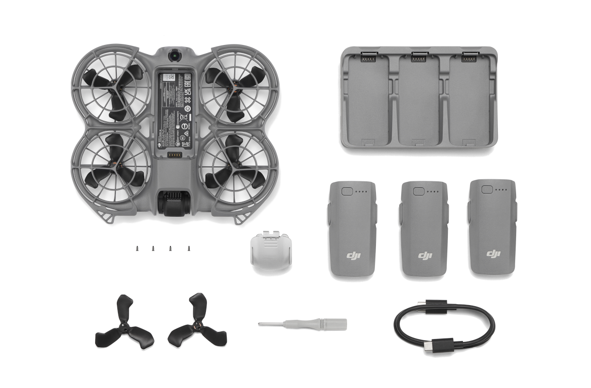 Elementy drona na czarnej powierzchni. Zawiera drona, baterie, ładowarkę, śmigła, śrubokręt i kabel ładujący.
