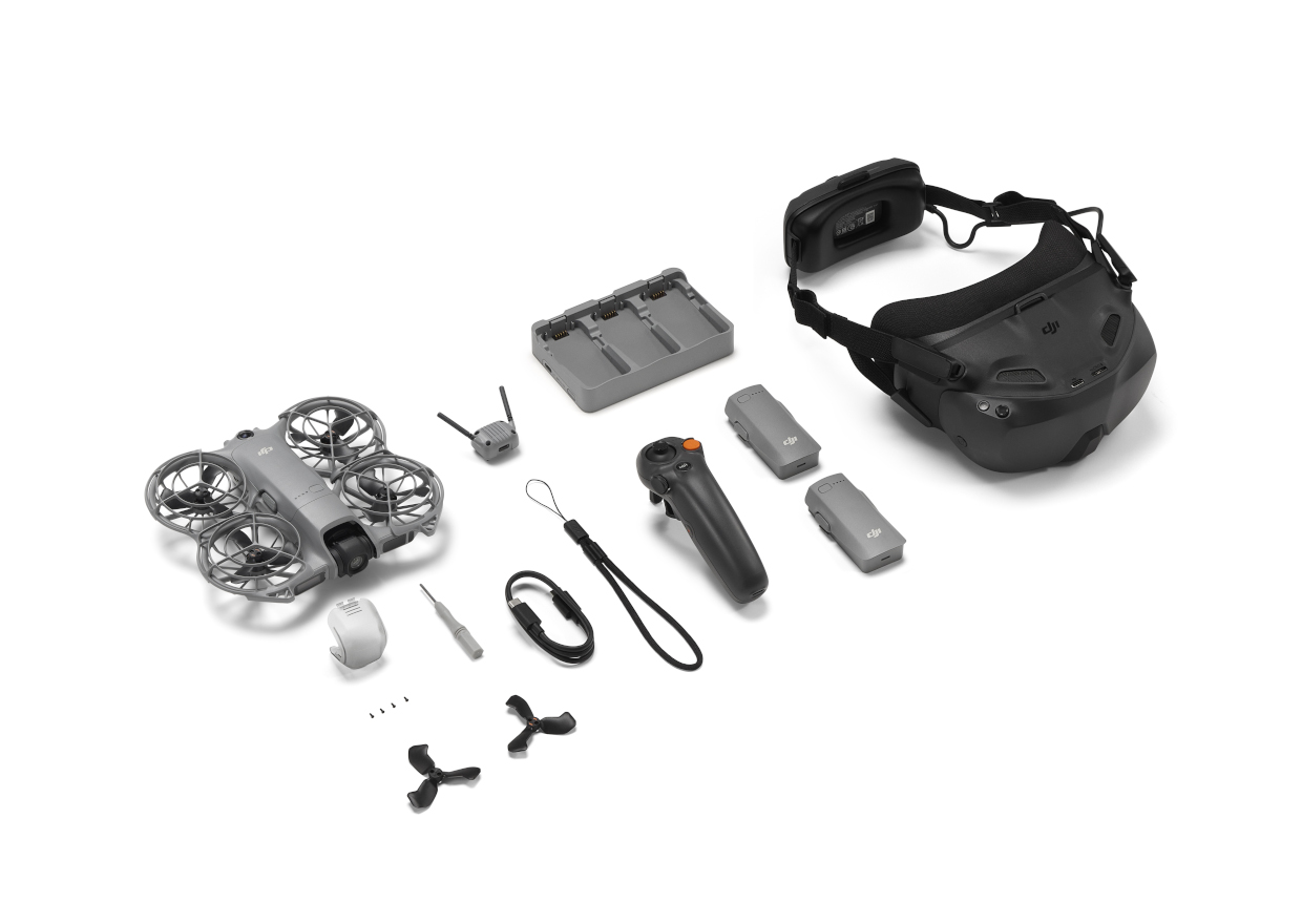 Dron, gogle, kontroler, baterie, ładowarka i akcesoria na białym tle. Wszystko jest szare lub czarne.