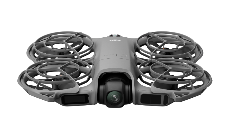 Szary dron z czterema śmigłami, klatkami ochronnymi i kamerą na czarnym tle.