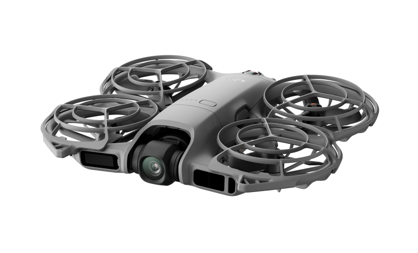 Szary dron z czterema śmigłami, kamerą i klatkami ochronnymi wokół śmigieł jest odizolowany na czarnym tle.