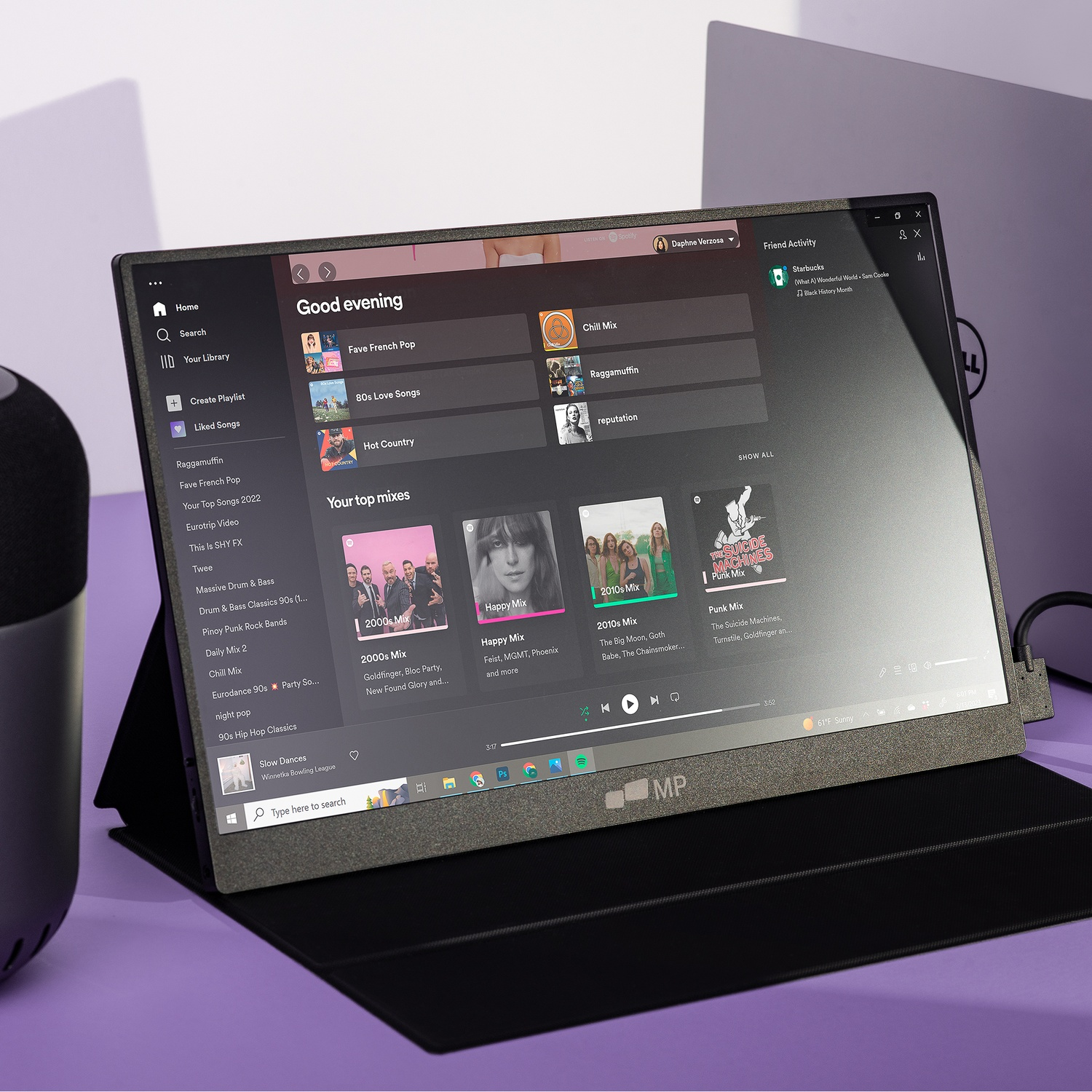 Laptop displays a music app, showing playlist options and song suggestions, with a purple background and a speaker.