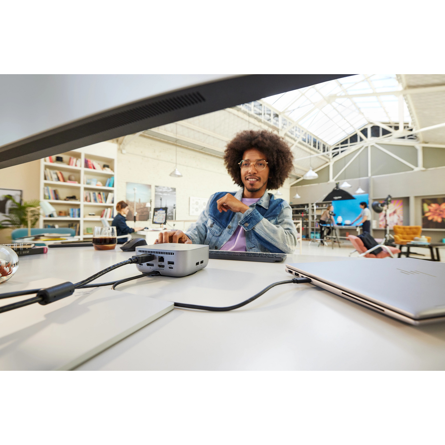 A man with glasses and afro works on a computer. A silver computer is in front of him. A laptop is on the right.