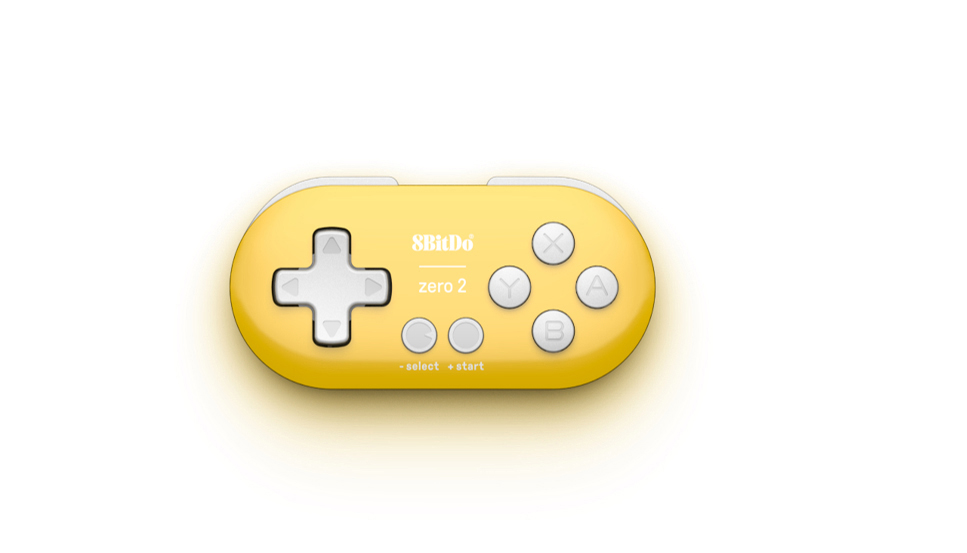 Ein gelbes und weißes 8BitDo Zero 2 Gamepad liegt auf einer weißen Oberfläche. Es hat Knöpfe und ein Steuerkreuz. Der Hintergrund ist weiß.