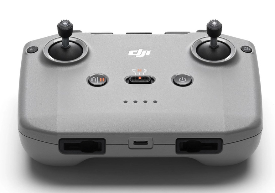 Szary kontroler drona z dwoma joystickami, przyciskami i portami. Widoczne logo DJI. Kontroler jest na białym tle.