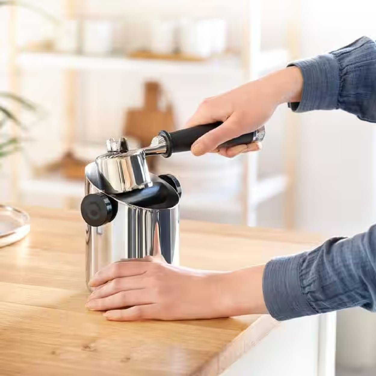 Una persona usa una macchina per caffè espresso argentata. Una mano tiene la maniglia, l'altra stabilizza la macchina.