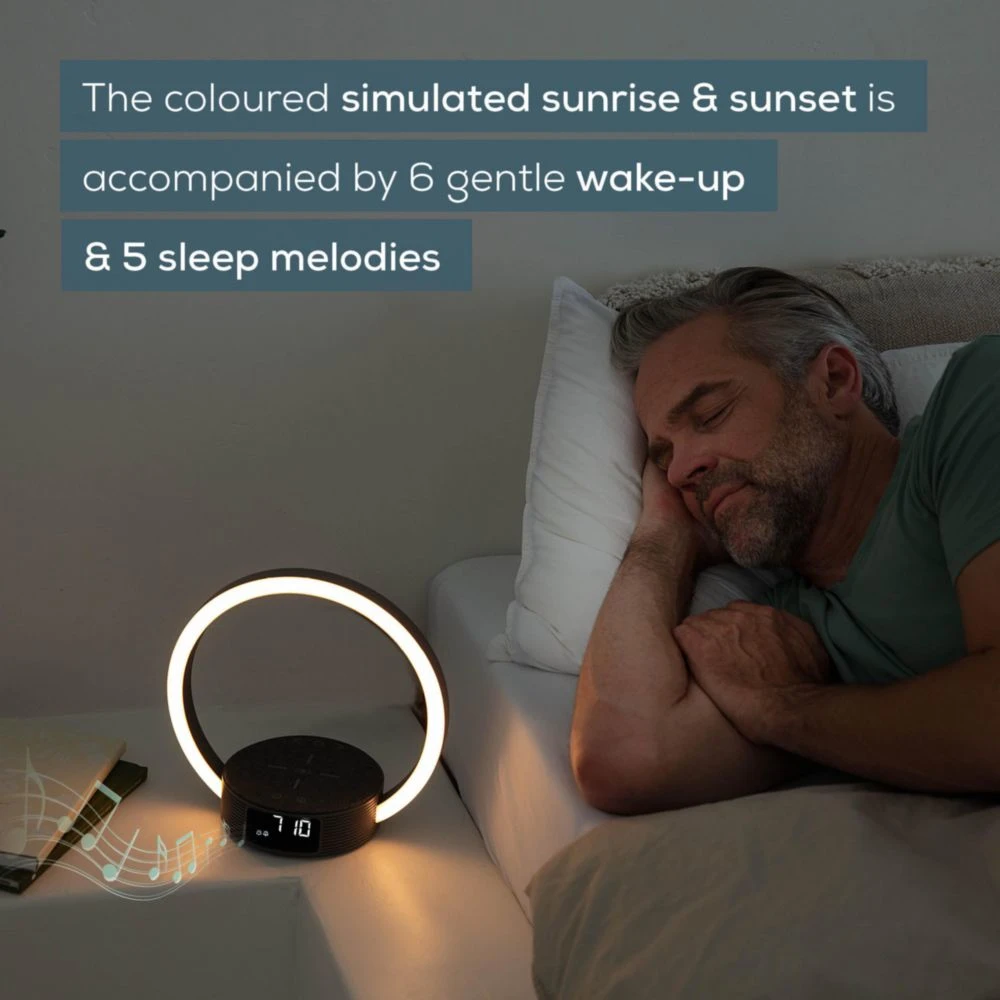 Un homme dort dans son lit. Une lampe de chevet avec un anneau lumineux est allumée. Texte : lever et coucher de soleil, 6 réveils et 5 mélodies.