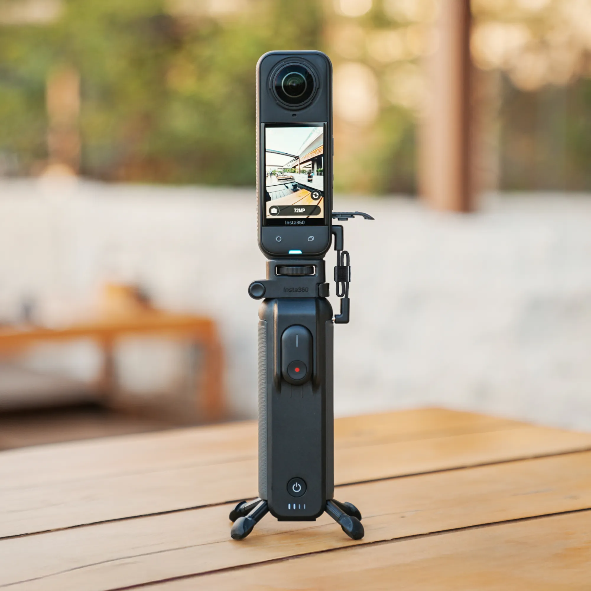 Schwarze Insta360-Kamera auf einem Stativ. Der Bildschirm zeigt eine Ansicht. Die Kamera steht auf einem Holztisch mit unscharfem Hintergrund.
